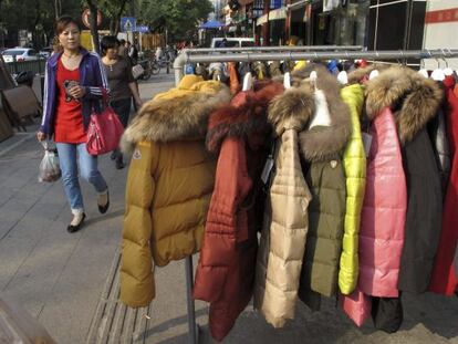 Una mujer pasa por delante de un comercio que expone ropa de invierno en Pek&iacute;n.