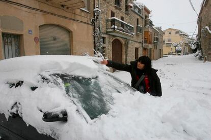 Una vecina de Belltall (Tarragona) trata de quitar la nieve de su coche.