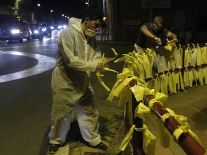 Dos hombres retiran lazos amarillos en Girona.