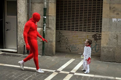 Un niño vestido de blanco y rojo como manda la tradición de los Sanfermines se sorprende al ver a un hombre cubierto íntegramente con un traje rojo, en una calle de Pamplona.