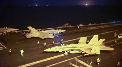 Cazabombarderos Hornet y Super Hornet se preparan para una misión nocturna en la cubierta del USS Truman. Al fondo se ve la llama de un pozo petrolífero.