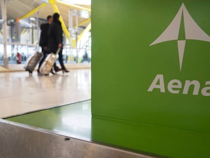 Dos viajeros pasan ante un cartel de Aena en el aeropuerto de Madrid-Barajas.