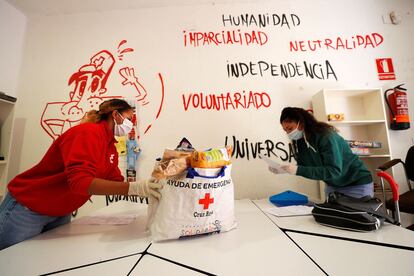 Una voluntaria de Cruz Roja entrega una bolsa con productos de primera necesidad a una joven en Valencia. / MANUEL BRUIQUE (Efe)