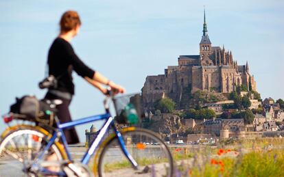 Una mujer pasea con su bicicleta frente al Mont Saint-Michelle, en Francia.