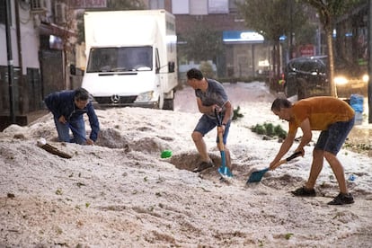 Tres vecinos limpian de granizo una de las calles de la localidad madrileña de Arganda del Rey, tras la fuerte tormenta de lluvia y granizo que ha caído este lunes en toda la Comunidad de Madrid.