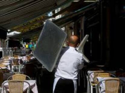 Un camarero recoge una mesa de una terraza de un restaurante del barrio de la Barceloneta de Barcelona.