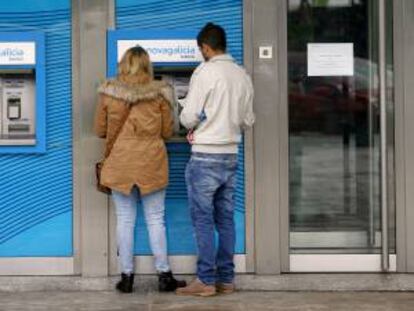 Dos jóvenes retiran dinero de un cajero en una sucursal de Novagalicia Banco. EFE/Archivo