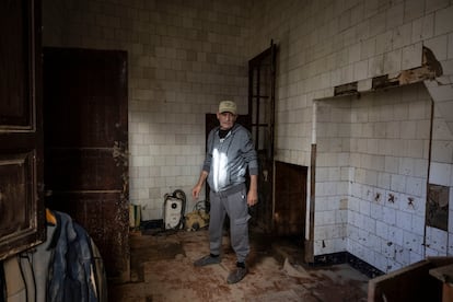 Gabriel, ciudadano español de origen rumano, posa en Pedralba, frente a su vivienda gravemente afectada por la riada del 29 de octubre. En la misma calle Acequia, una placa recuerda el nivel alcanzado por el agua durante la histórica riada de 1957, a 2,5 metros del suelo, un paralelismo que evidencia la magnitud del desastre actual. Gabriel, albañil y residente en España desde hace casi dos décadas, relata cómo tuvo que abandonar su casa esa noche, nadando entre barro y cañas, sin poder salvar casi nada. De todas sus pertenencias, solo logró recuperar su DNI español. 