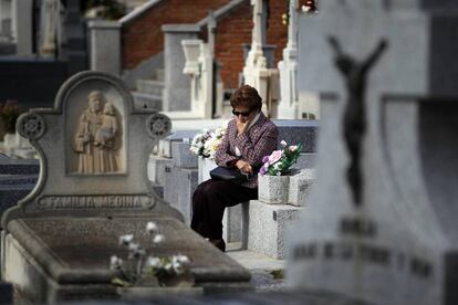 Una mujer reflexiona sentada sobre una tumba en el cementerio.