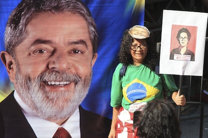 Mulher segura foto de Dilma diante de cartaz que exibe Lula.