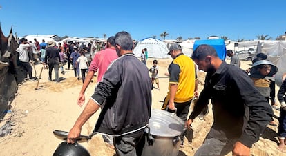 Un grupo de gazatíes lleva ollas y sartenes para recibir los pocos alimentos que llegan a Al Mawasi, donde se han desplazado tras la ofensiva israelí.
