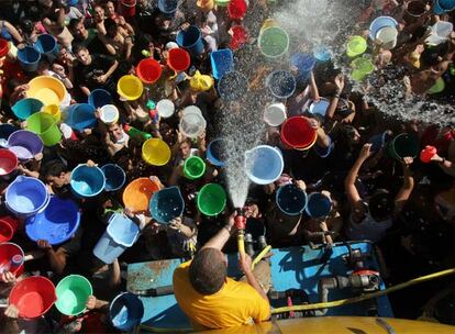 Vecinos de Vallecas, pertrechados de cubos, tratan de llenarlos del agua que sale de una manguera.