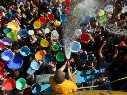 Vecinos de Vallecas, pertrechados de cubos, tratan de llenarlos del agua que sale de una manguera.