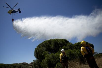 Un retén mira como un helicóptero tira agua a un rebrote del fuego cercano al Parador Nacional de Mazagón.