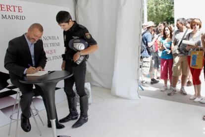 Arturo Pérez-Reverte firma un ejemplar a un policía nacional, mientras una larga fila espera.