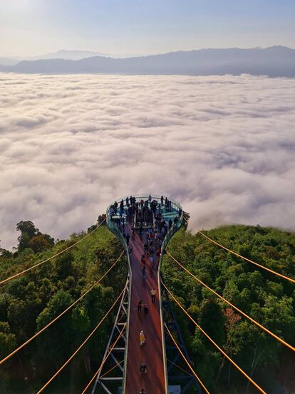 Al amanecer y al atardecer, las brumas cubren los bosques tropicales de la colina de Ai Yerweng, en el distrito de Betong en Yala, una de las tres provincias meridionales de Tailandia, de mayoría de población musulmana, en un país donde la religión oficial es el budismo. En su cima se alza uno de los miradores más espectaculares del sudeste asiático, una pasarela de 61 metros de largo —y un final con suelo acristalado— a 621 metros de altura, inaugurada en 2020. Cerrada por la pandemia el pasado abril, tiene previsto reabrir de nuevo al público este mes de diciembre, cuando Tailandia se dispone a permitir el acceso libre al país a los turistas con la pauta completa de vacunación. El mirador pretende atraer a los turistas locales y extranjeros a la región y, al mismo tiempo, crear oportunidades de trabajo entre la población local.