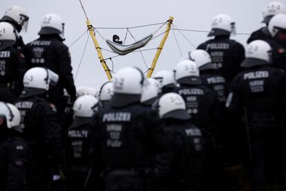 Decenas de agentes observan a un manifestante que descansa en una hamaca instalada a varios metros de altura, en Lützerath este martes. 
