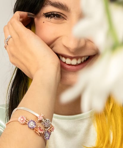 Cariatydes posa con la Pulsera Pandora Moments en Pandora Rose Multicadena de Serpiente, llena de los nuevos charms Pandora Rose Margarita Rosa y Margarita Morada en plata de Ley, y la pulsera Moments en plata de ley, reiventada con los clip Pandora Rose Margarita Rosa, el charm en plata de ley Margarita Morada Filigrana o el charm en filigrana Pandora Rose Margarita. En la mano, el anillo Corona de Margaritas Brillantes y el anillo en Pandora Rose Solitario Morado.