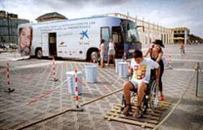 Un chico comprueba las dificultades de quienes se mueven en silla de ruedas junto al autobús de la accesibilidad, en Valencia.