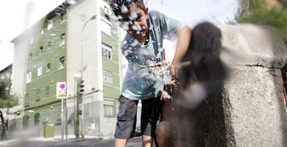 Un niño juega con el agua de una fuente en el barrio de San Blas, en Madrid.