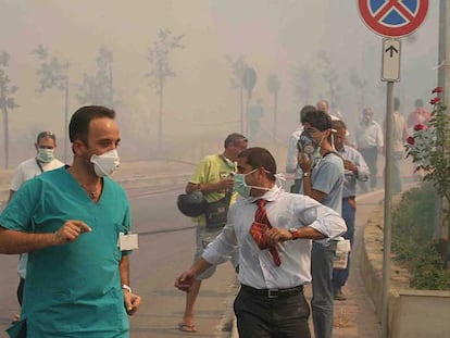 Decenas de personas se protegen del humo con mascarillas al ser evacuadas de un hospital  de Cefalú.
