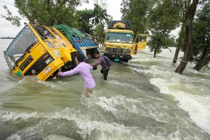 Un grupo de hombre pasa junto a dos camiones varados en una calle inundada en Sunamganj, Bangladés, este martes. Las inundaciones son una amenaza habitual para millones de personas en las zonas bajas del país, pero los expertos dicen que el cambio climático está aumentando su frecuencia, ferocidad e imprevisibilidad.