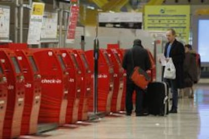 Varios pasajeros junto a unos mostradores de facturaci&oacute;n autom&aacute;ticos en la T4 del aeropuerto de Barajas.