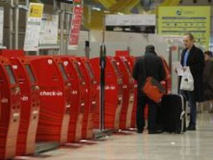 Varios pasajeros junto a unos mostradores de facturaci&oacute;n autom&aacute;ticos en la T4 del aeropuerto de Barajas.