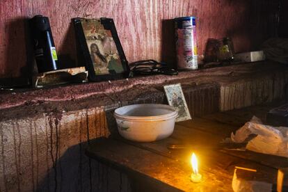 La imagen 'La última luz', en Orocovis, Puerto Rico, 2017. Una pequeña vela descansa encendida encima de una mesa de madera, rodeada de una tarjeta de santo, fotos familiares y vasos.