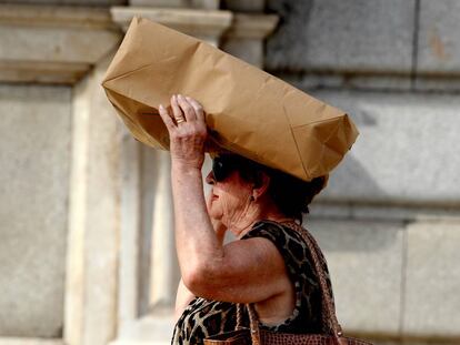 Una mujer se cubre la cabeza con una bolsa debido al fuerte sol en una ola de calor en Madrid.