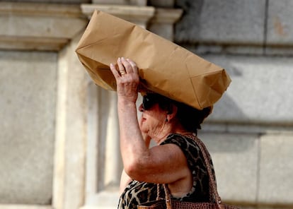 Una mujer se cubre la cabeza con una bolsa debido al fuerte sol en una ola de calor en Madrid.