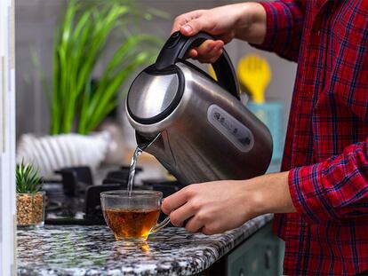 Un hombre echando agua del hervidor a una taza de té.