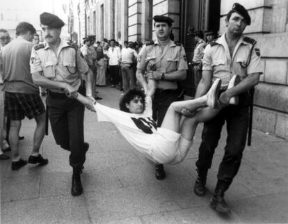 Tres agentes de la Policía Nacional llevan en volandas a una joven que participó en los actos de protesta contra el servicio social sustitutorio organizado por el Movimiento de Objeción de Conciencia (MOC) en la Puerta del Sol, ante la sede del Gobierno autonómico en Madrid.