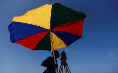 Un topógrafo toma medidas para un nuevo proyecto de vía férrea debajo de una sombrilla, en la playa de Colombo (Sri Lanka), el 16 de noviembre.