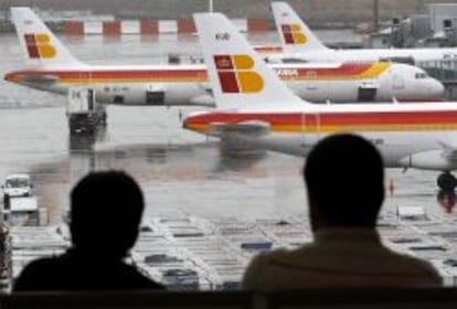 Dos pasajeros observan varios aviones de la compa&ntilde;ia Iberia en las pistas del aeropuerto de Barajas.