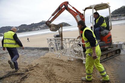 Trabajadores del Ayuntamiento de San Sebastián retiran una barandilla derribada tras el fuerte oleaje en la playa de La Concha.