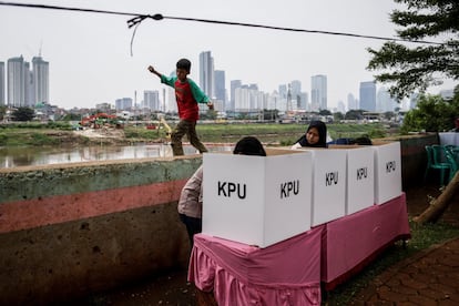 Un niño camina sobre un muro junto a una mesa electoral en Yakarta.