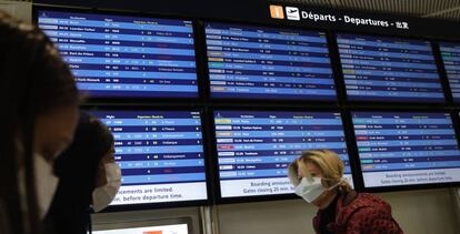 Varias personas con mascarillas pasan frente a un tablón de salidas del aeropuerto París-Orly el martes 17 de marzo. 