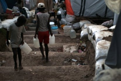 Dos mujeres caminan con garrafas de agua por uno de los campamentos donde viven personas que se quedaron sin hogar tras el terremoto del 12 de enero.