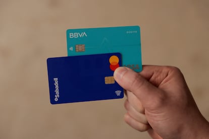 Un hombre muestra sus tarjetas de créditos del BBVA y del Banco Sabadell.