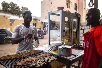 Abdou y Abdoulaye preparan las brochetas mientras esperan a que llegue la clientela. “La gente va con mucha prisa, sobre todo estos días con la Copa de África. Todos quieren llegar a casa para ver el partido, por eso vamos preparando las brochetas para que, cuando lleguen, se las lleven recién hechas”, afirma Abdoulaye.