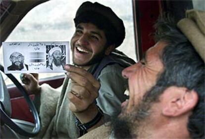 Dos milicianos ríen mientras muestran las fotos de Omar y Bin Laden junto a sus recompensas, a su regreso de Tora Bora sin lograr encontrarlos.