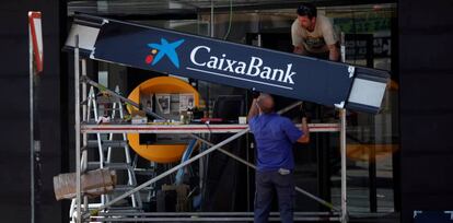 Operadores colocan un cartel Caixabank en la apertura de una nueva oficina