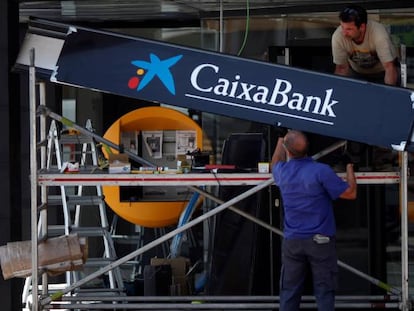 Operadores colocan un cartel Caixabank en la apertura de una nueva oficina