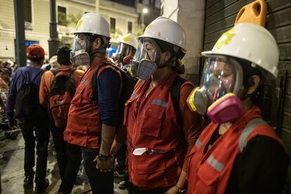 Tres brigadistas con máscaras para cuidarse del gas pimienta y una camilla, pegados a la pared de una calle limeña durante una protesta.