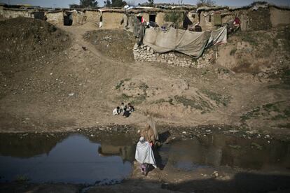 Unas mujeres cruzan un arroyo contaminado mientras unos niños juegan en un campamento de refugiados a las afueras de Islamabad (Paquistán).