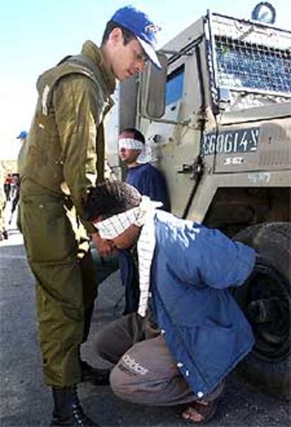 Un soldado israelí vigila a dos palestinos detenidos ayer en Hebrón.