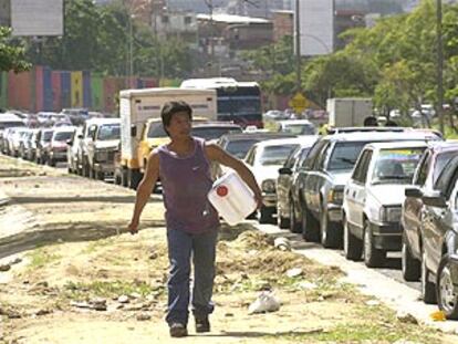 Un hombre camina con un bidón hacia una gasolinera de Caracas ante una cola de coches que van a repostar.