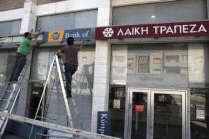 Dos trabajadores retiran el cartel del banco "Laikí" (Banco Popular) y lo reemplazan por el del Banco de Chipre, en Nicosia (Chipre). EFE/Archivo