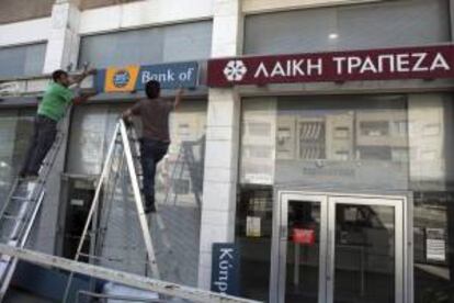 Dos trabajadores retiran el cartel del banco "Laik" (Banco Popular) y lo reemplazan por el del Banco de Chipre, en Nicosia (Chipre). EFE/Archivo